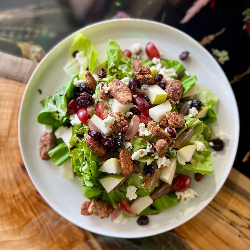 A vibrant Feast and Graze salad with greens, pears, grapes, candied pecans, and feta cheese.